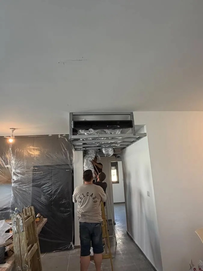 שלד מתכת להנמכת תקרה סביב תעלות מיזוג, עם עובדים על סולם